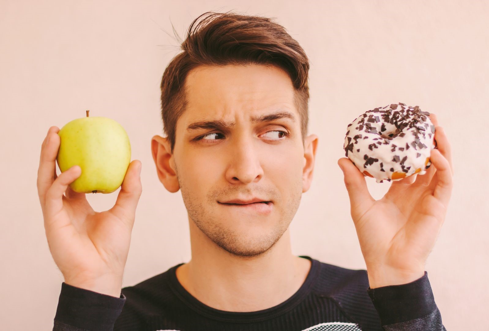 Homme hésitant entre une pomme et un donuts