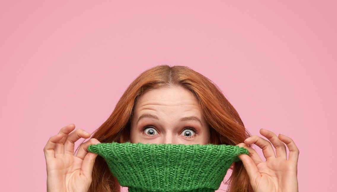 Femme rousse se cachant le visage avec un pull vert